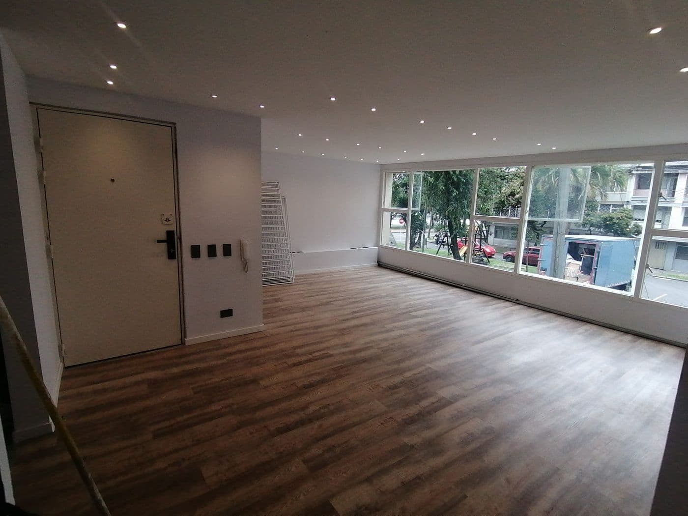 Sala amplia con ventanal corrido, luces empotradas en el cielo raso y piso laminado oscuro